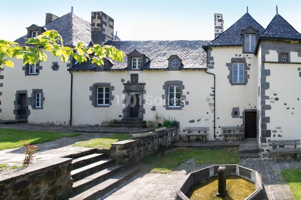 Façade d'une maison en pierre de style traditionnel avec toit en ardoise, entourée d'un jardin verdoyant.