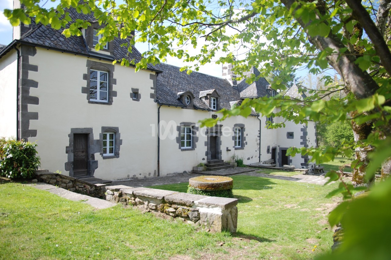 Façade d'une maison en pierre de style traditionnel, entourée de verdure et éclairée par la lumière du jour.