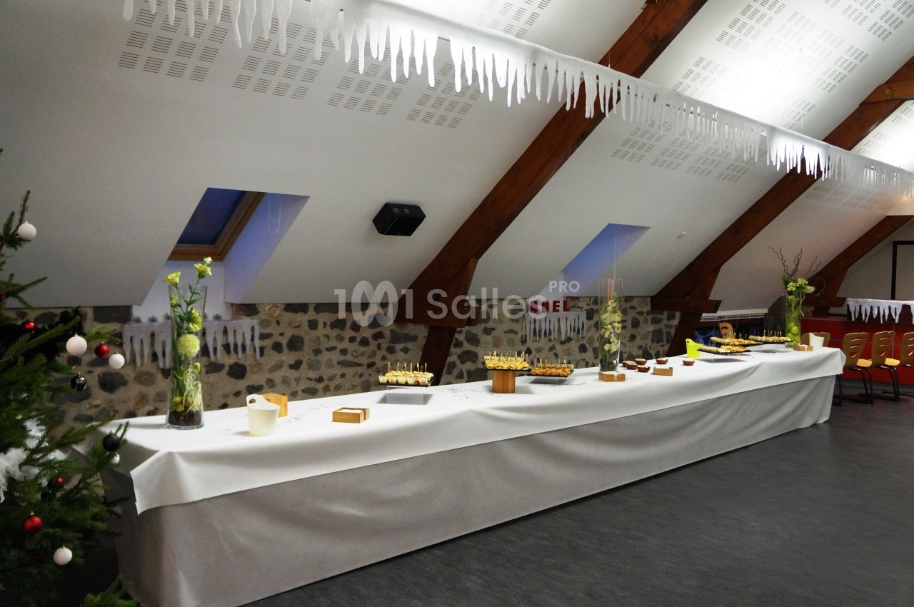 Table de buffet décorée sous un plafond mansardé avec des poutres en bois, ornée de fleurs et de plats variés.
