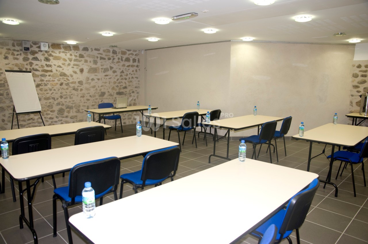 Salle de réunion avec tables et chaises disposées en rangées, bouteilles d'eau et tableau de présentation.