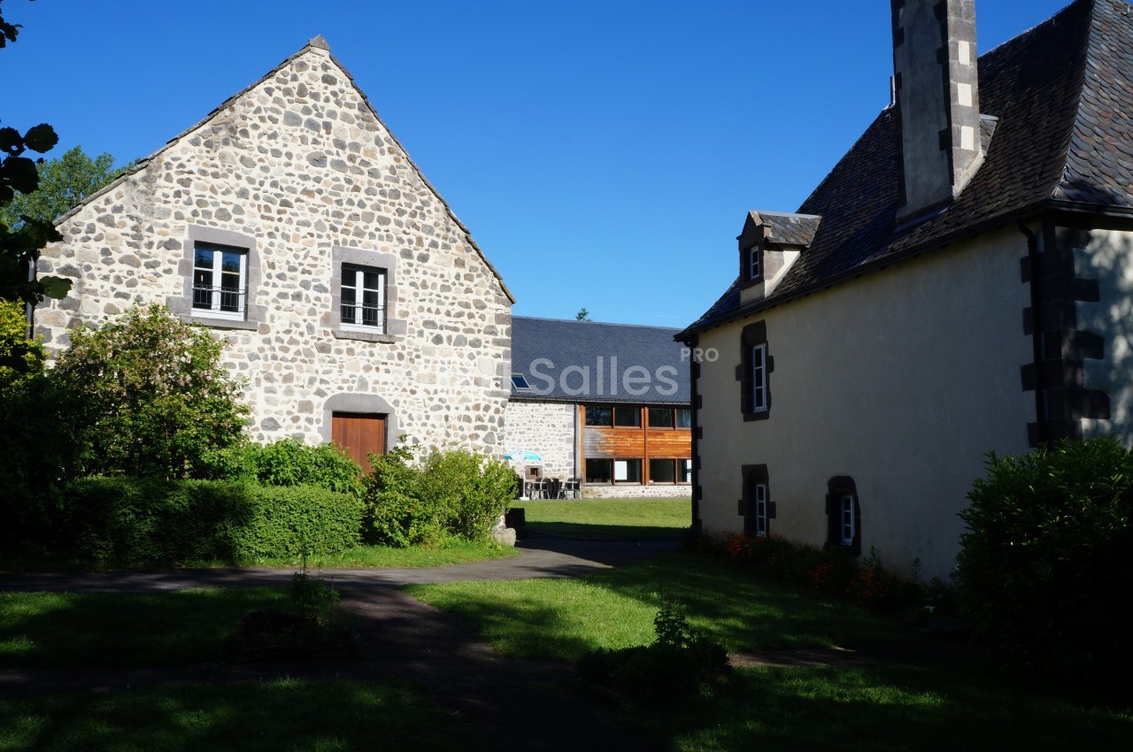 Deux bâtiments en pierre avec jardin verdoyant sous un ciel bleu clair.