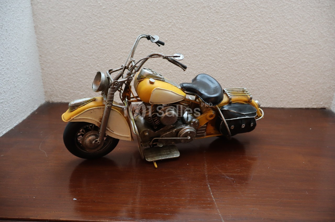 Modèle réduit de moto vintage jaune avec détails métalliques, posé sur une surface en bois.