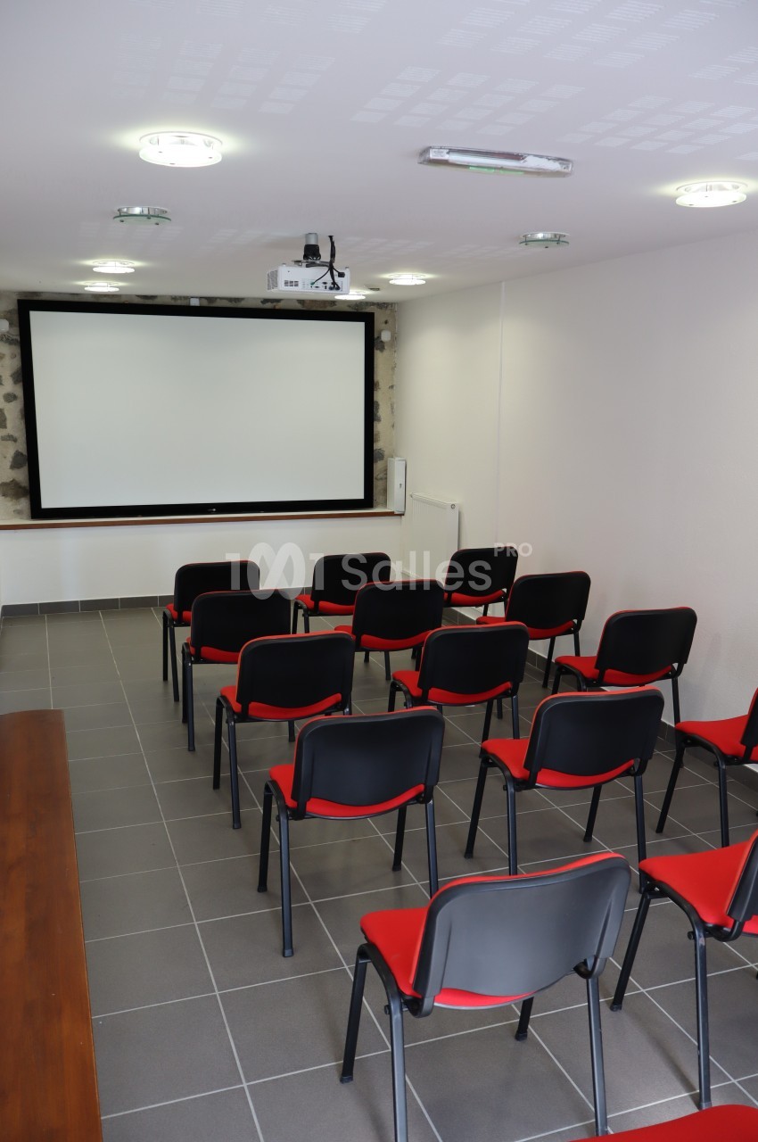 Salle de réunion équipée de chaises rouges et noires, d'un vidéoprojecteur et d'un écran blanc.