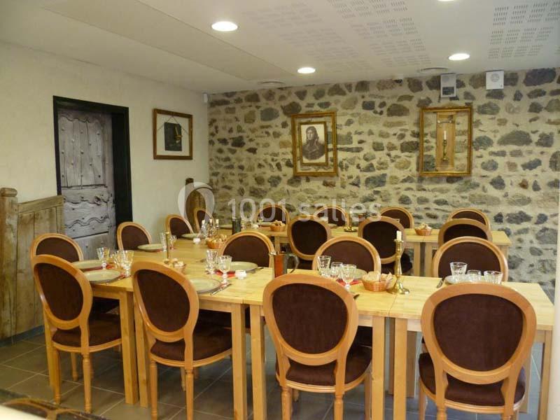 Salle de restaurant avec des tables en bois dressées, chaises à dossier rembourré et murs en pierre décorés de cadres.