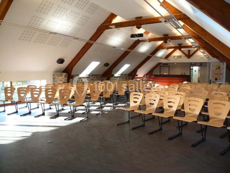 Salle de conférence lumineuse avec des rangées de chaises en bois et une charpente apparente.