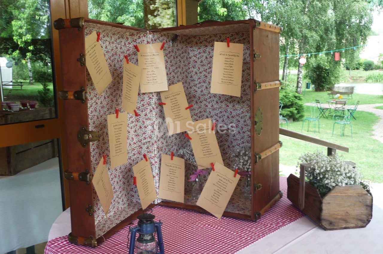 Vieille valise ouverte décorée de tissu fleuri, utilisée comme plan de table avec des cartons suspendus par des pinces.