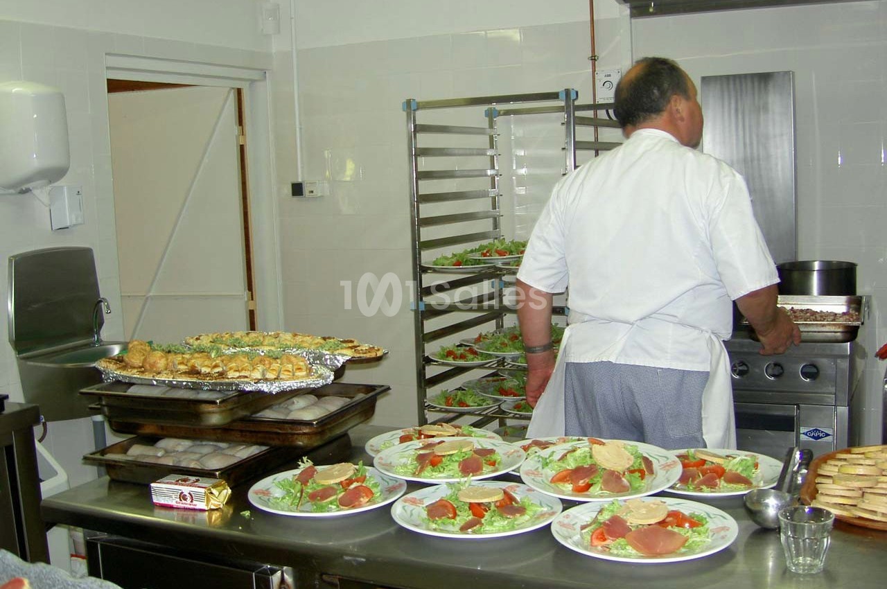 Un cuisinier prépare des plats dans une cuisine professionnelle avec des assiettes de salade prêtes à être servies.