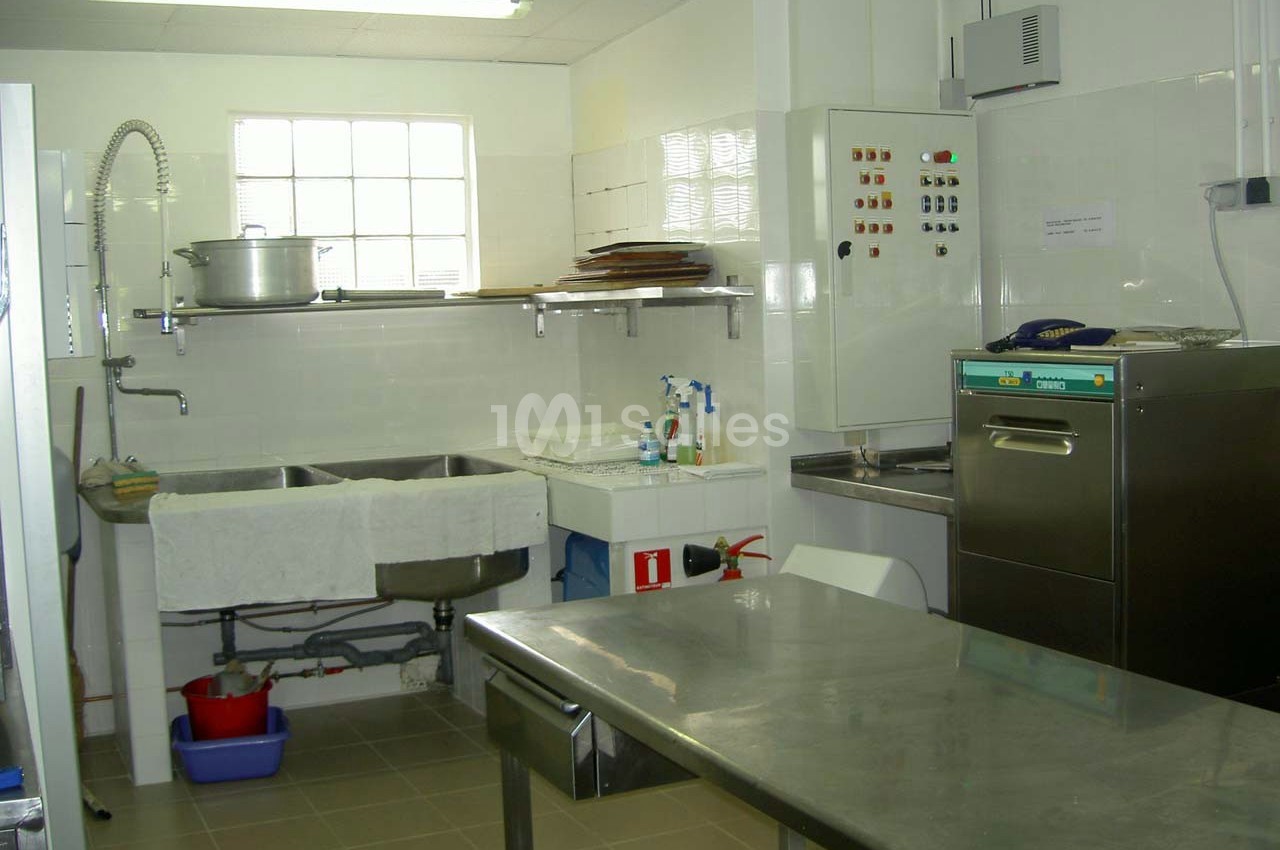 Cuisine professionnelle équipée avec évier double, plan de travail en inox, lave-vaisselle et étagères murales.