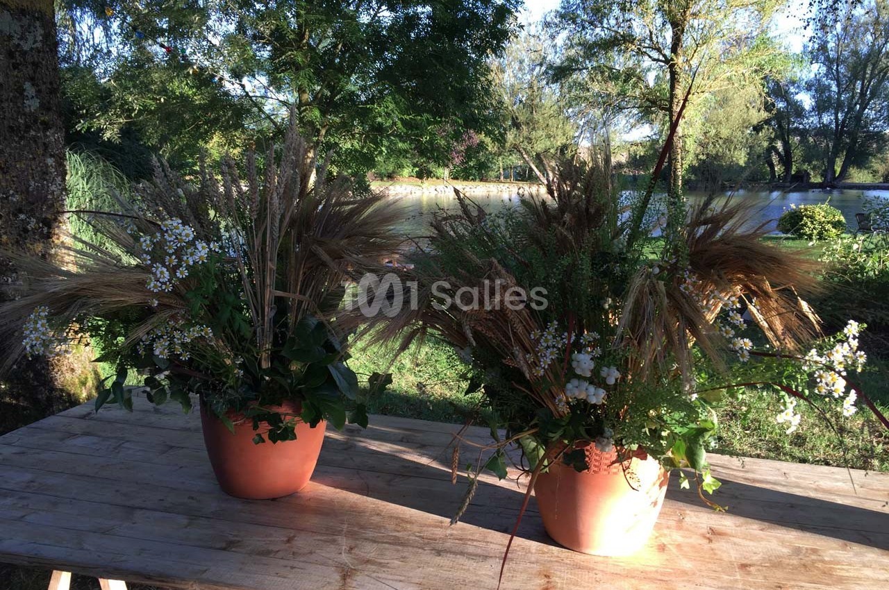 Deux pots en terre cuite contenant des compositions florales avec des herbes sèches et des fleurs blanches, posés sur une…