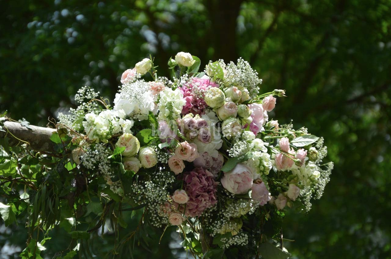 Bouquet de fleurs pastel avec des roses, hortensias et gypsophiles, suspendu devant un arrière-plan de verdure.