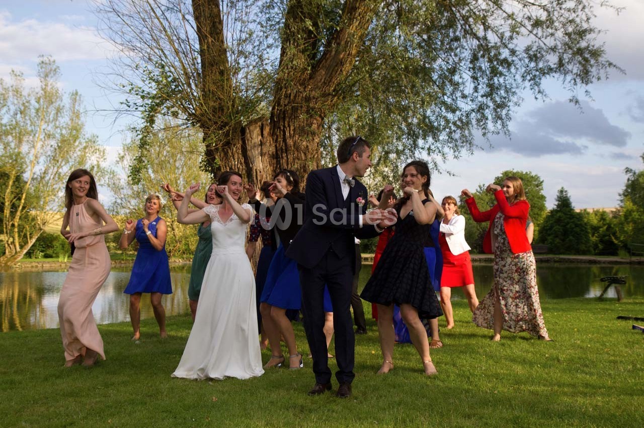 Des invités dansent en plein air près d'un arbre et d'un étang lors d'une célébration, avec une mariée au centre.