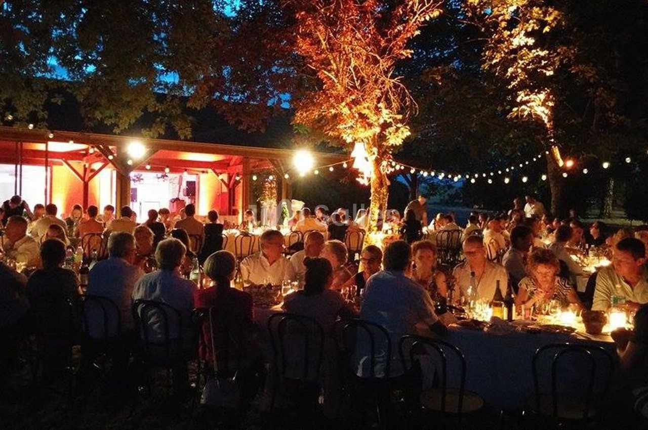 Groupe de personnes dînant en soirée dans un jardin éclairé par des guirlandes lumineuses et des lampes.