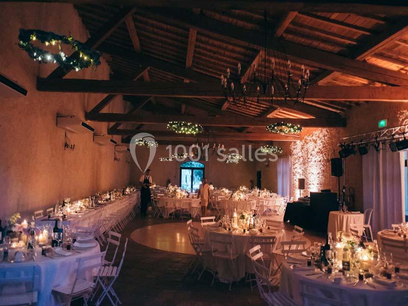 Salle de réception décorée pour un événement, avec tables dressées, bougies allumées et éclairage tamisé.