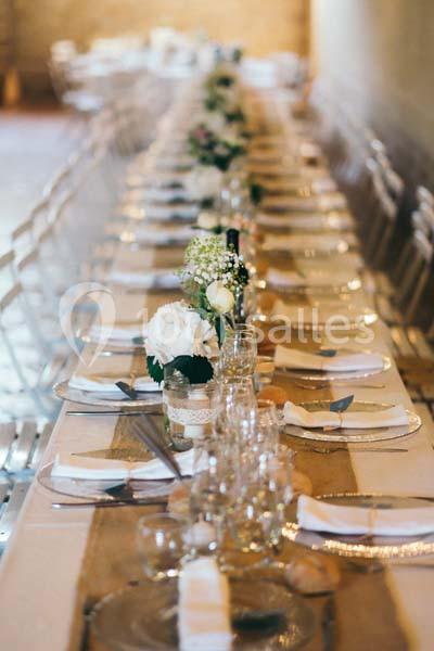 Table longue décorée pour un événement, avec nappes blanches, fleurs et vaisselle disposées de manière élégante.
