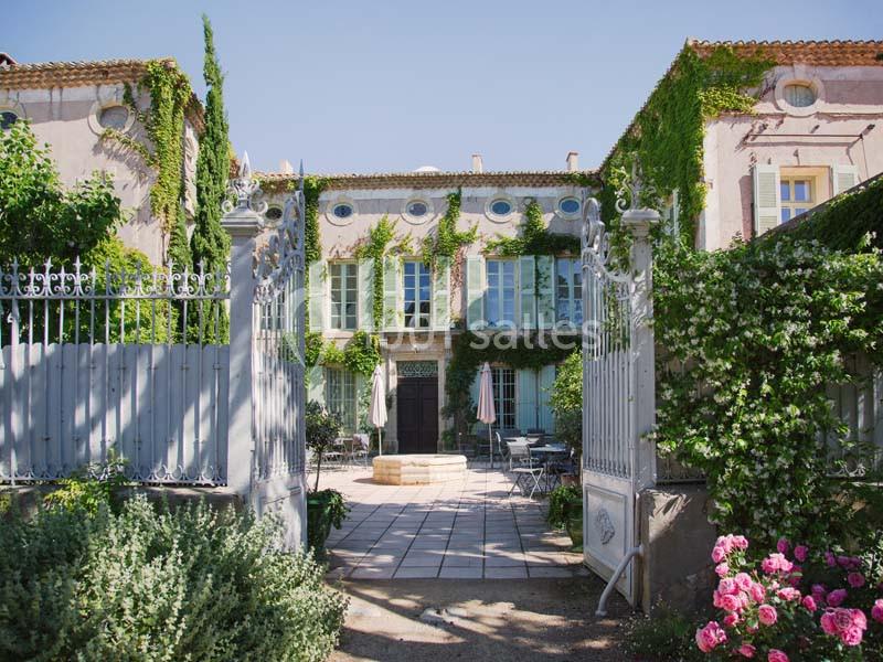 Façade d'une maison provençale entourée de végétation, avec une cour pavée et des meubles de jardin.
