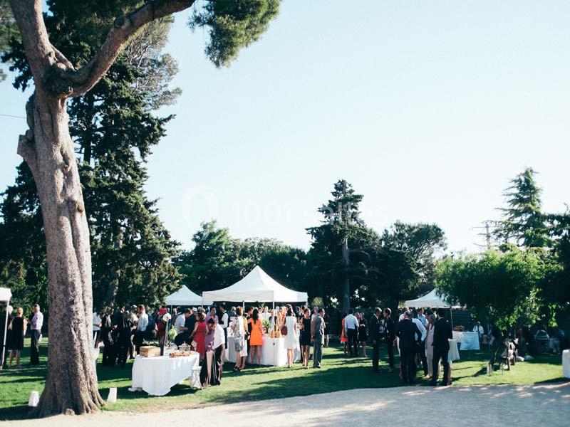 Groupe de personnes rassemblées dans un jardin avec des tentes blanches, entouré d'arbres et de verdure.