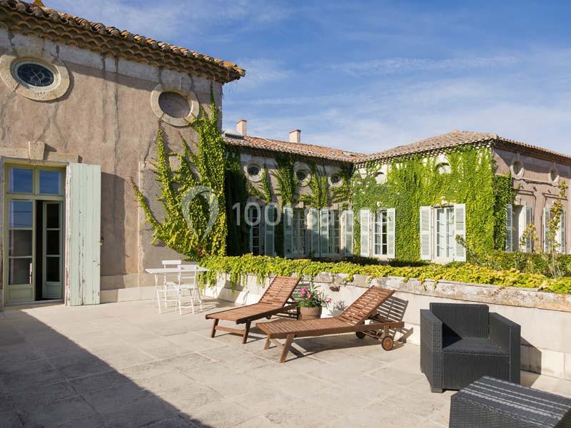 Terrasse ensoleillée avec chaises longues, mobilier d'extérieur et façade recouverte de vigne grimpante.
