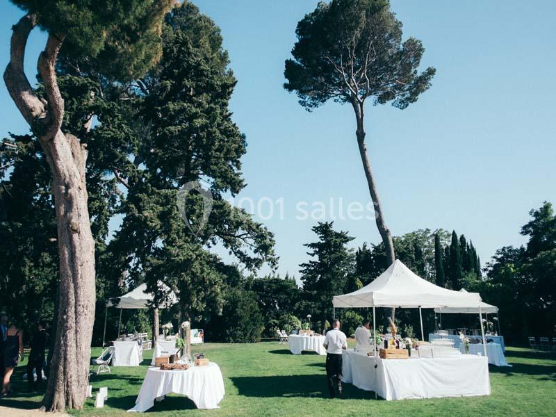 Des tables sous des tentes blanches sont installées dans un jardin verdoyant par une journée ensoleillée.