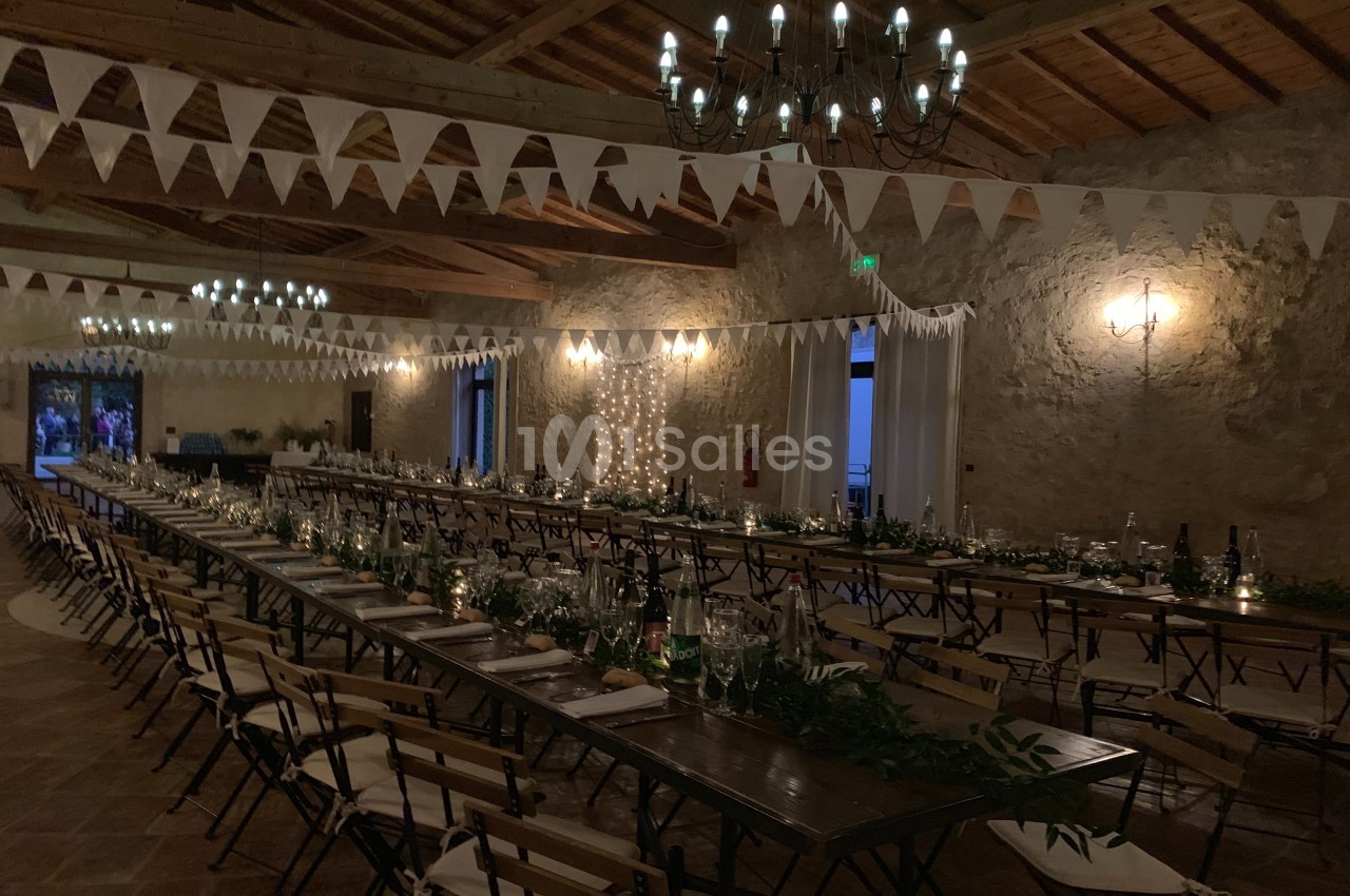 Grande salle décorée pour un événement, avec longues tables en bois, guirlandes lumineuses et fanions suspendus.