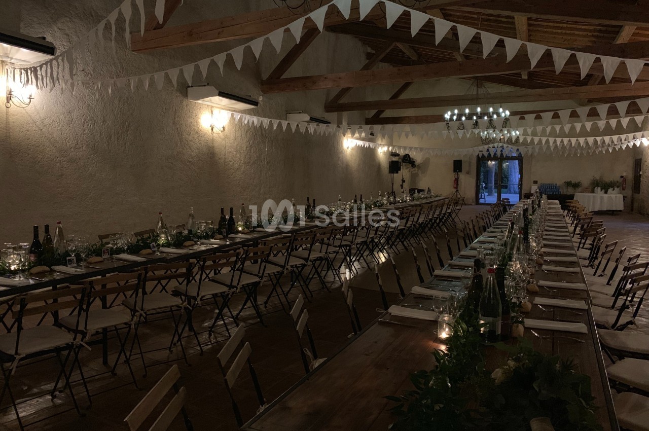 Grande salle décorée pour un événement, avec longues tables dressées, guirlandes de fanions et éclairage tamisé.