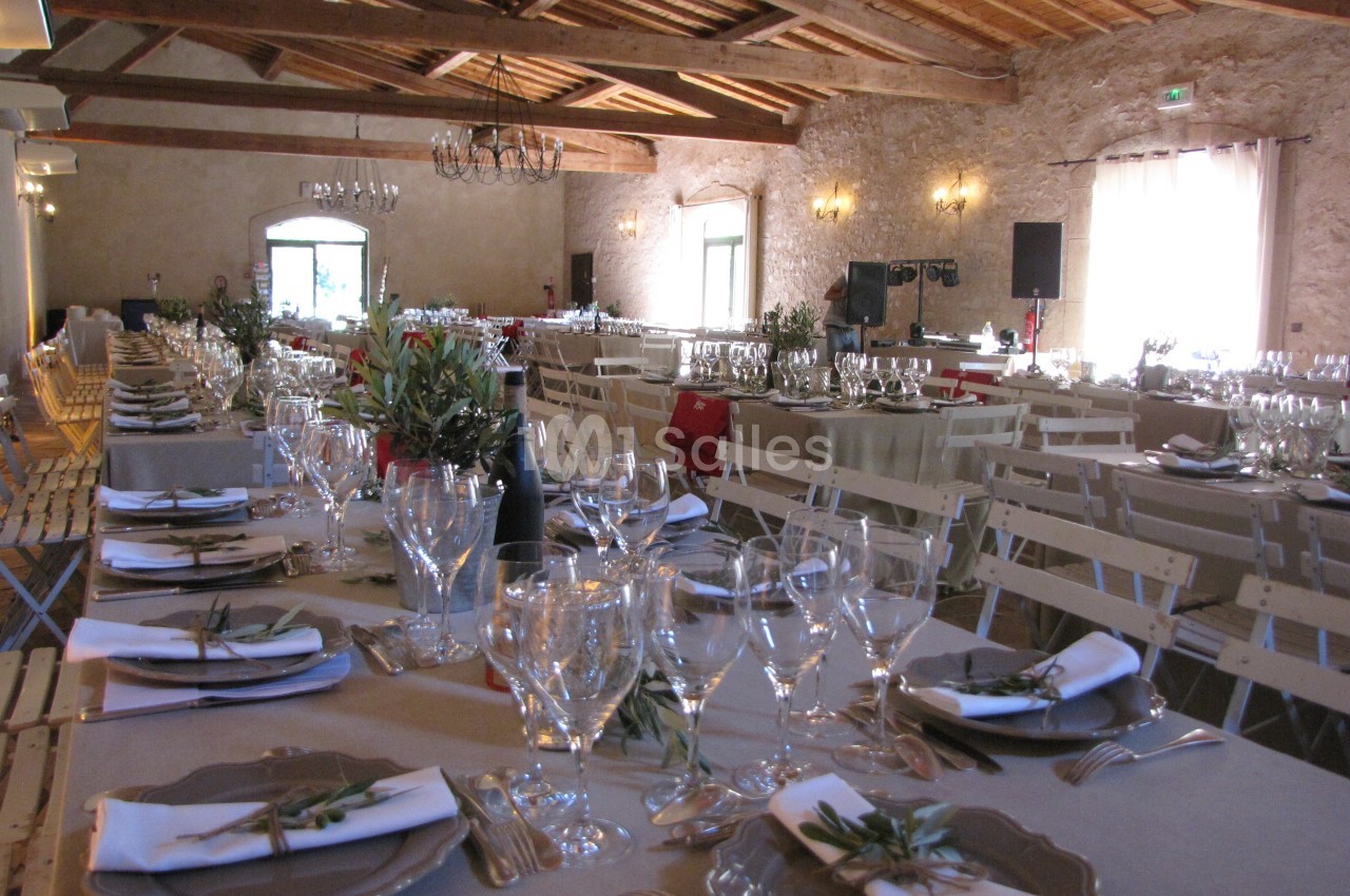 Salle de réception décorée avec des tables dressées, nappes beige, vaisselle élégante et branches d'olivier.
