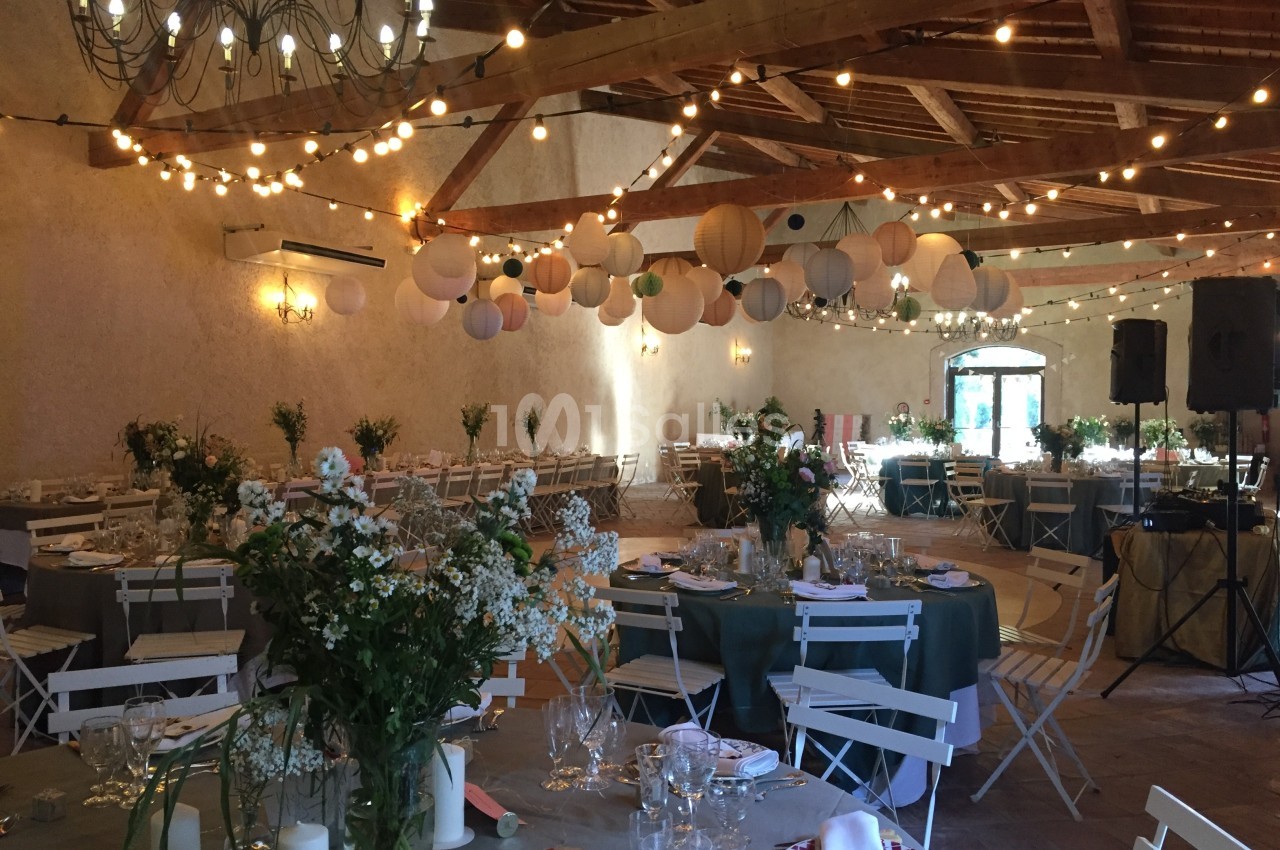 Salle de réception décorée avec des guirlandes lumineuses, des lanternes suspendues et des tables dressées avec des fleurs.