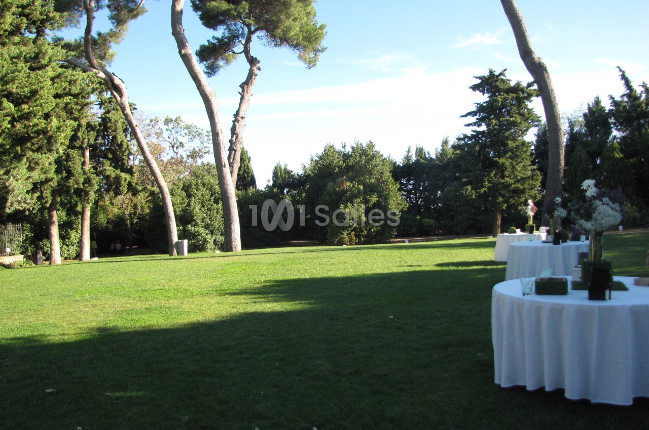 Pelouse verdoyante avec des tables rondes dressées en extérieur, entourée d'arbres et sous un ciel dégagé.