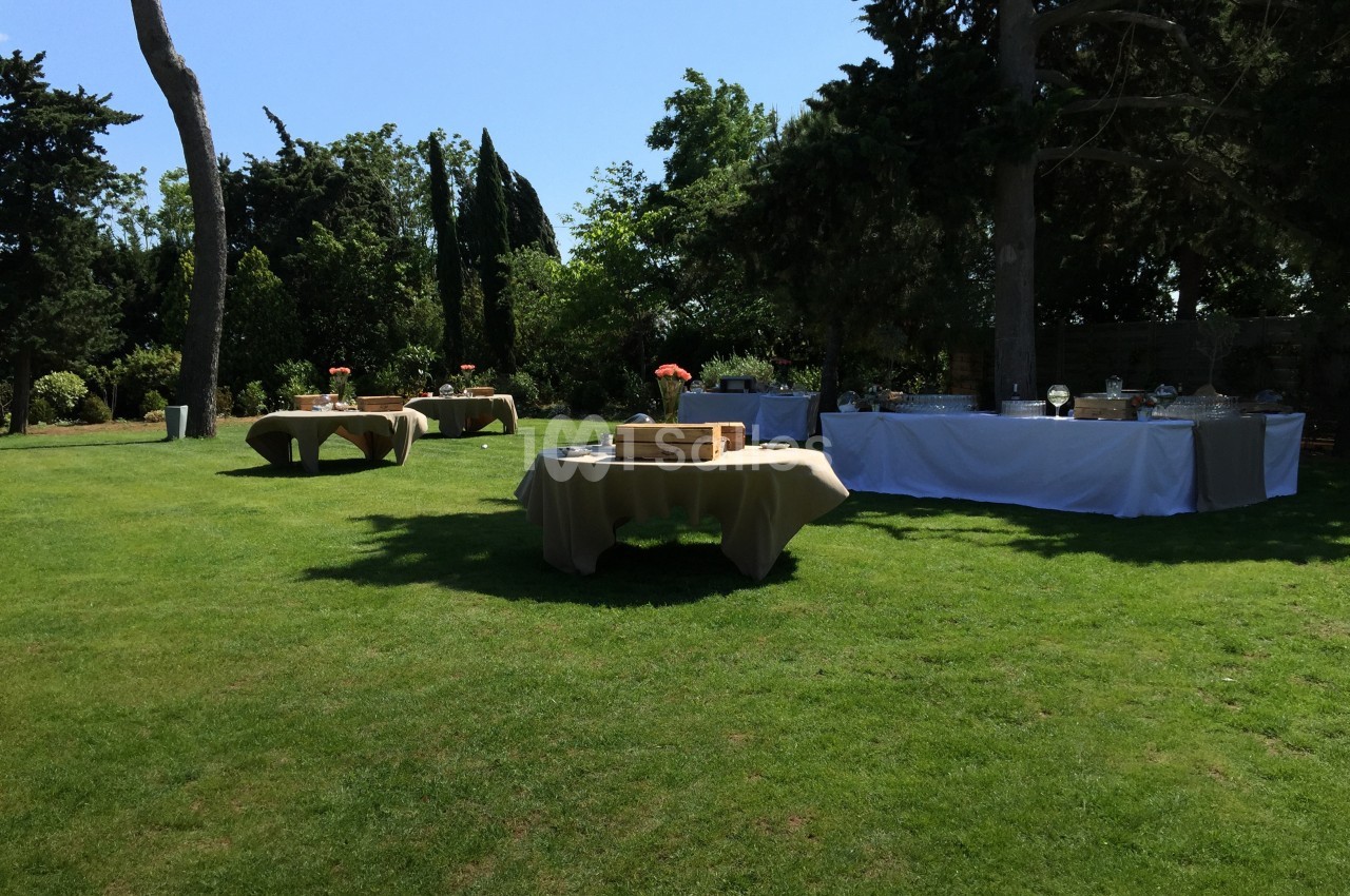 Tables dressées pour un événement en plein air sur une pelouse entourée d'arbres et de verdure.