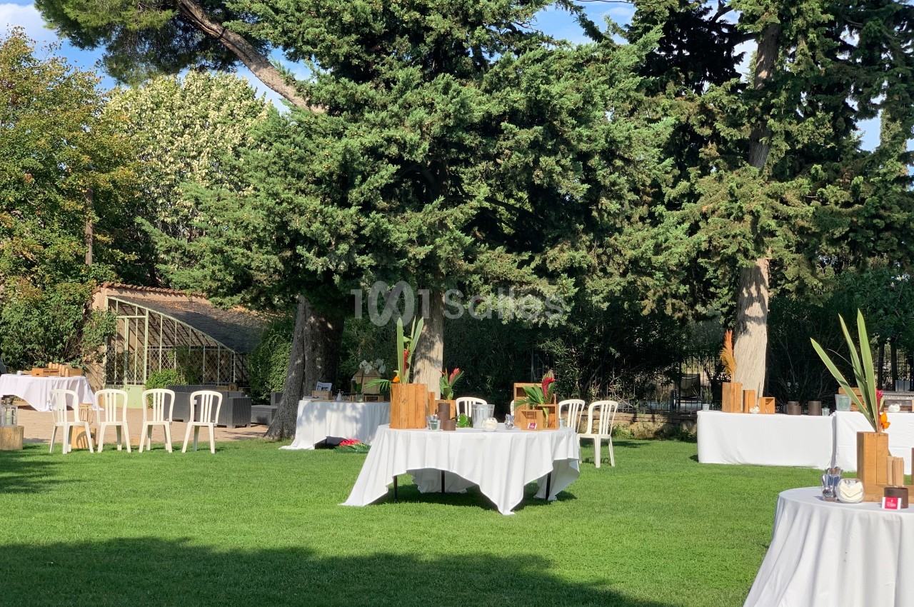 Tables décorées installées sur une pelouse entourée d'arbres, dans un jardin ensoleillé.