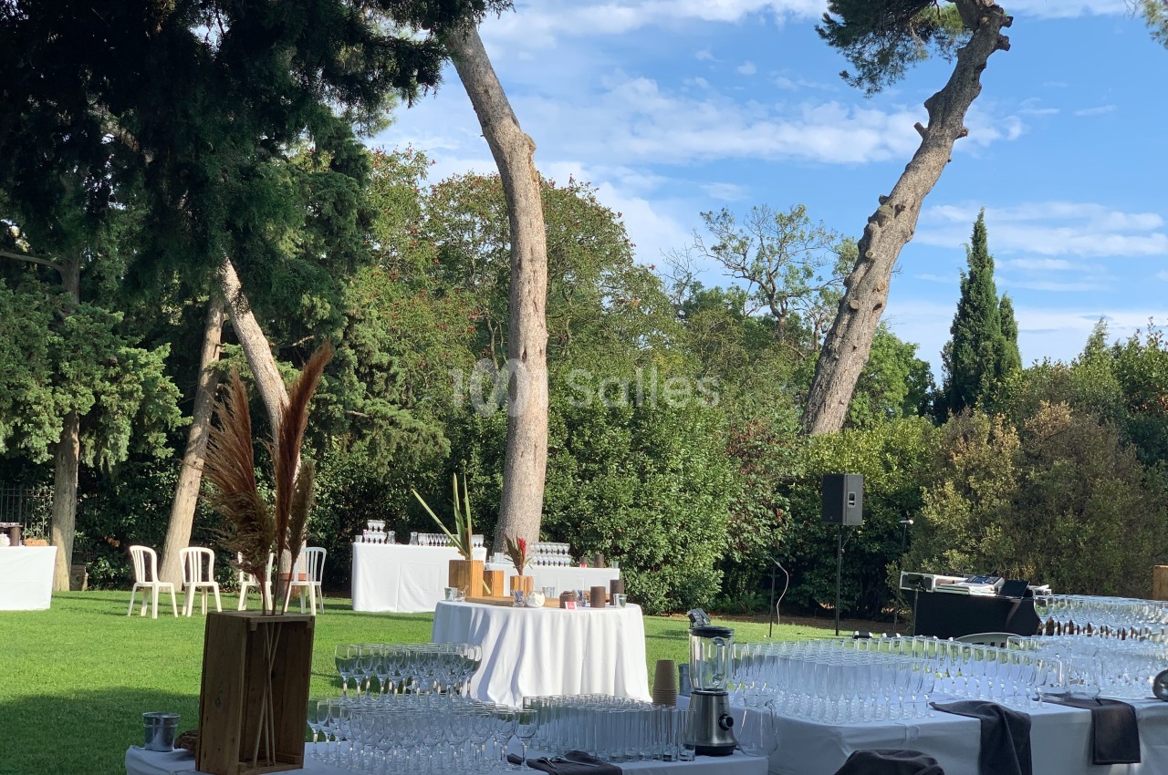 Tables dressées avec des verres et des décorations dans un jardin verdoyant sous un ciel bleu.
