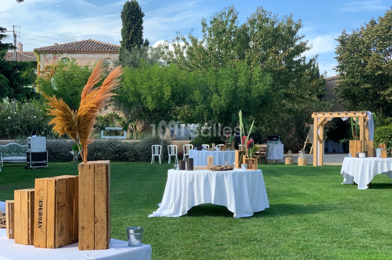 Tables décorées pour un événement en plein air, disposées sur une pelouse avec des éléments en bois et des plantes.