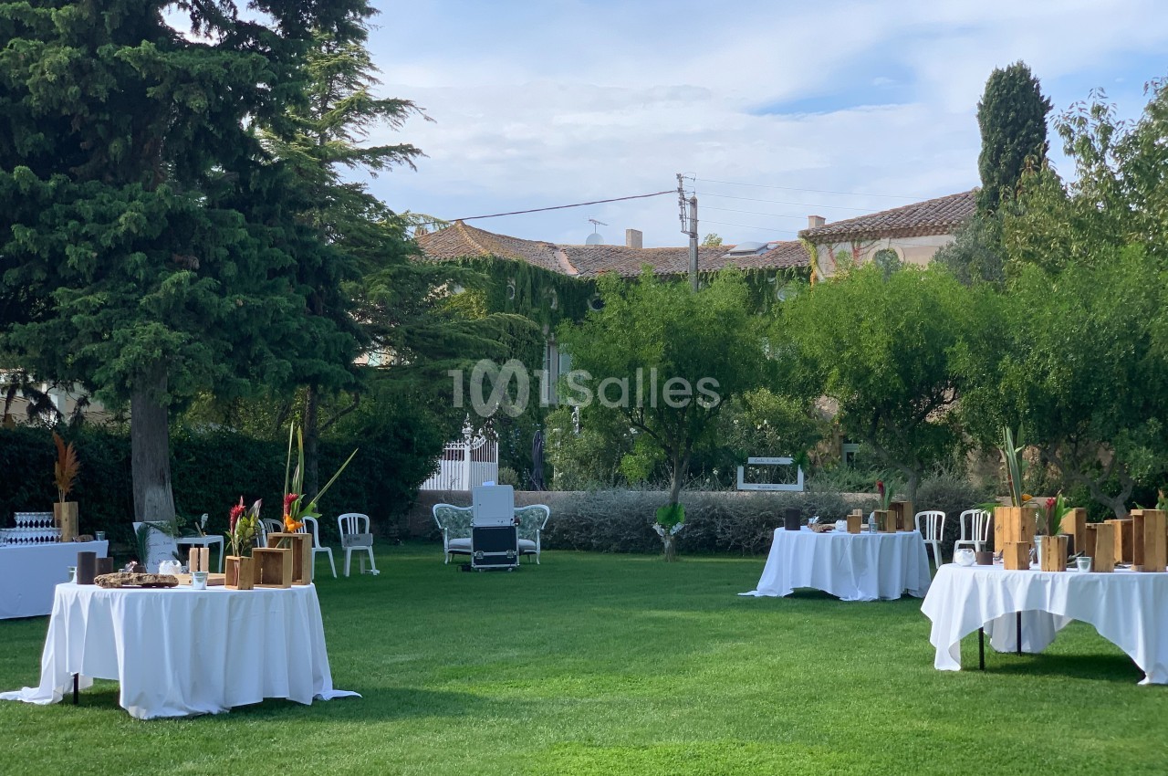 Tables dressées avec nappes blanches et décorations en bois disposées sur une pelouse dans un jardin arboré.