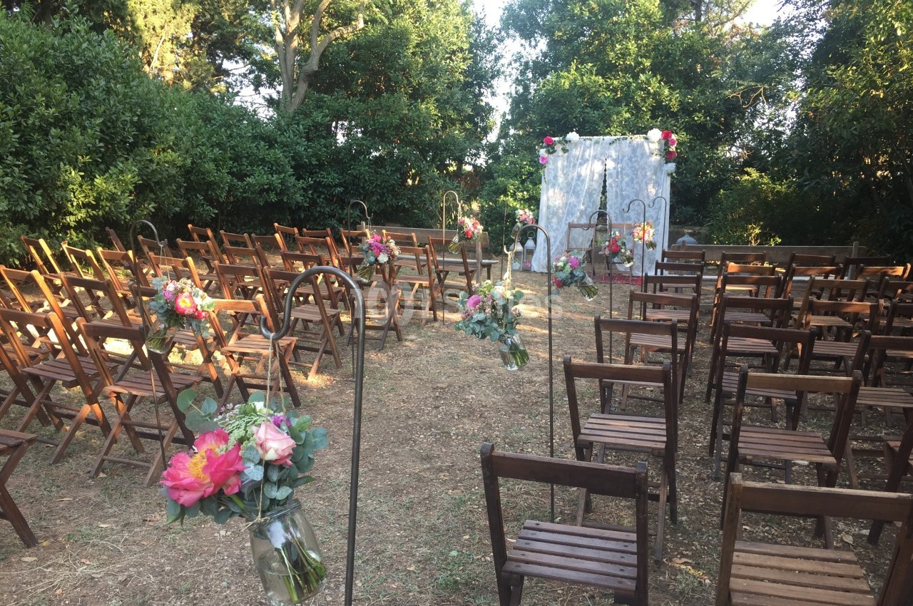 Chaises en bois disposées en rangées dans un jardin, décorées de fleurs, face à une arche ornée pour une cérémonie.