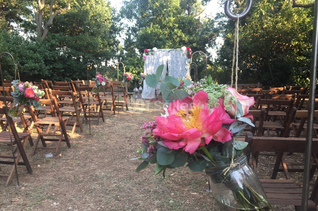Allée de chaises en bois décorées de fleurs colorées, menant à une arche pour une cérémonie en extérieur.