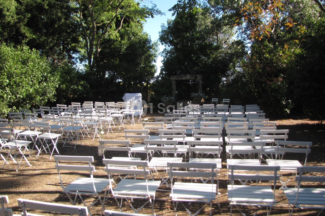 Chaises blanches disposées en rangées dans un espace extérieur entouré d'arbres, préparé pour un événement.