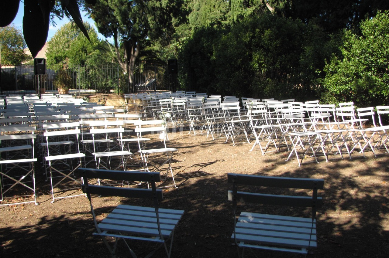 Chaises blanches pliantes disposées en rangées dans un espace extérieur entouré de végétation.