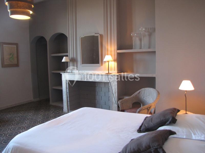 Chambre avec lit double, cheminée décorative, étagères intégrées, fauteuil en osier et éclairage doux.