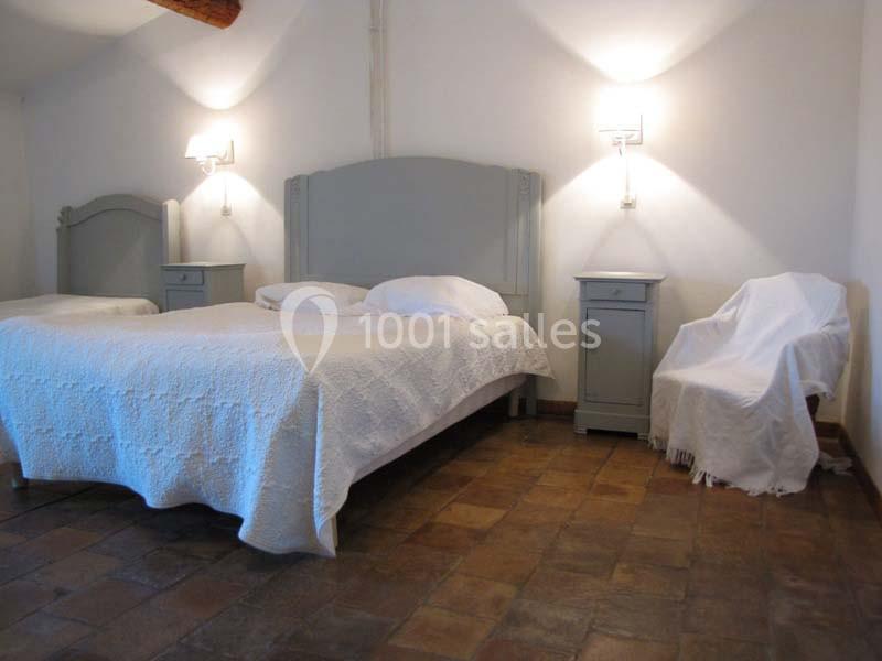 Chambre avec lit double, chevets assortis, fauteuil recouvert et sol en carrelage dans un décor sobre et lumineux.