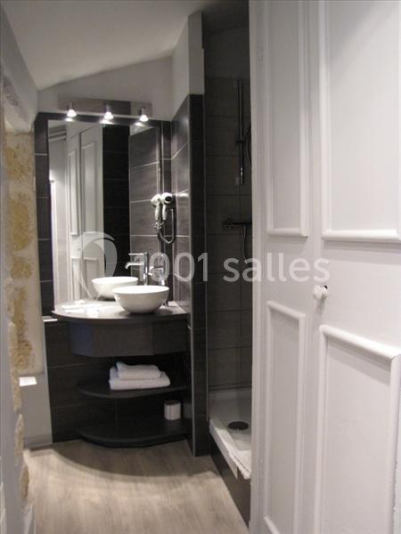Salle de bain moderne avec lavabo double, miroir éclairé, douche et étagères avec serviettes pliées.