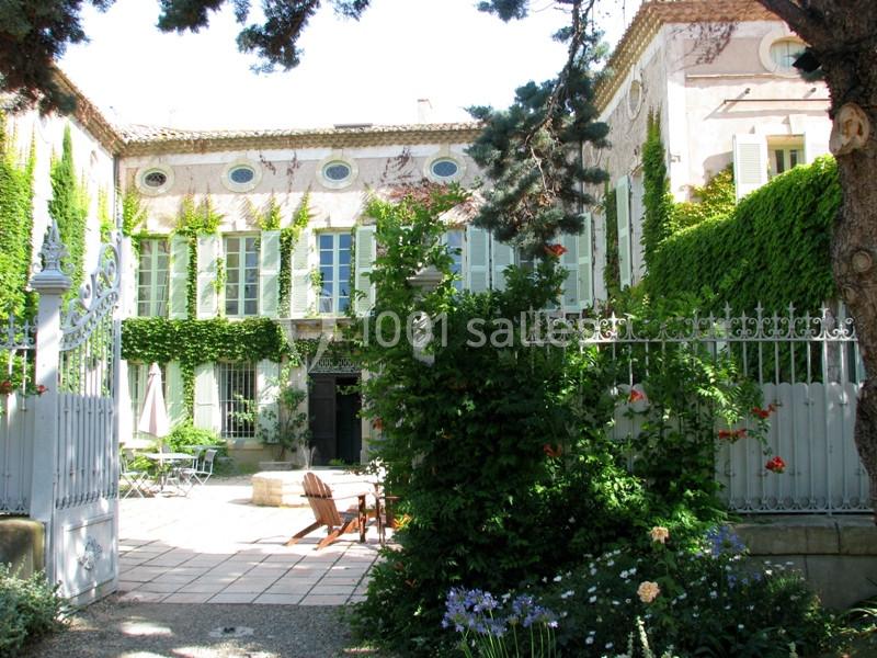 Façade d'une maison en pierre couverte de lierre, entourée d'un jardin avec des arbres, fleurs et mobilier de terrasse.