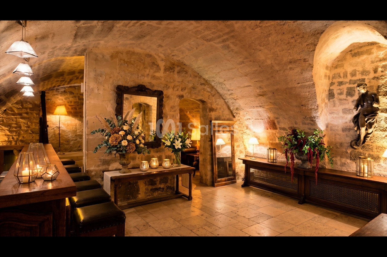 Salle voûtée en pierre avec éclairage chaleureux, décorée de fleurs, bougies et meubles en bois sombre.