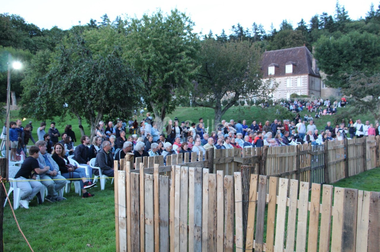 Un groupe de personnes assises en plein air devant une maison ancienne, entourées d'arbres et de barrières en bois.