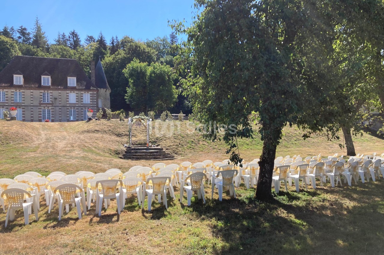 Chaises blanches disposées en rangées sur une pelouse, face à une arche décorative, avec un manoir en arrière-plan.