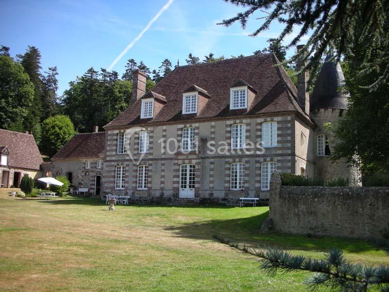Grande maison en pierre avec toit en ardoise, entourée de pelouse et d'arbres, avec une tour sur la droite.