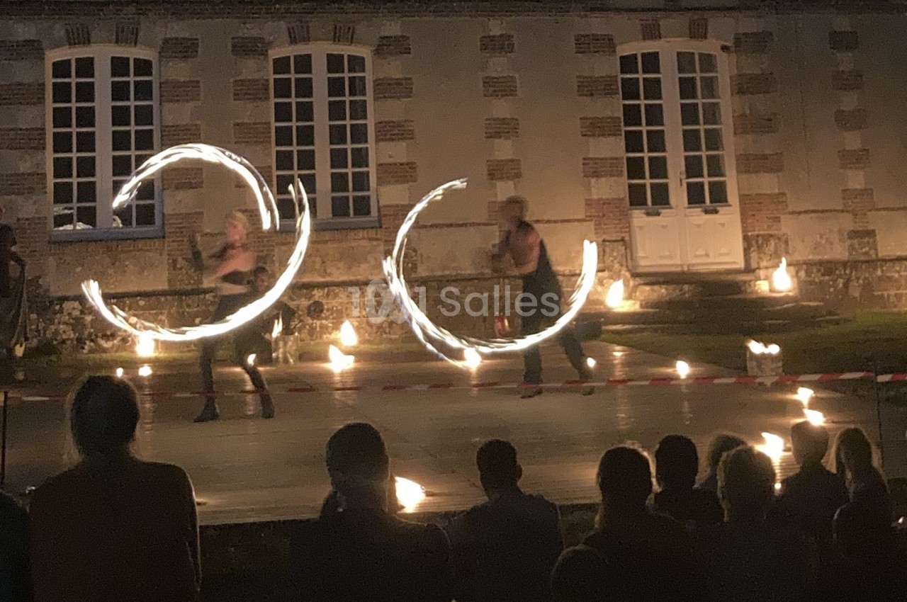 Deux artistes réalisent un spectacle de jonglage avec du feu devant un bâtiment en pierre, de nuit.