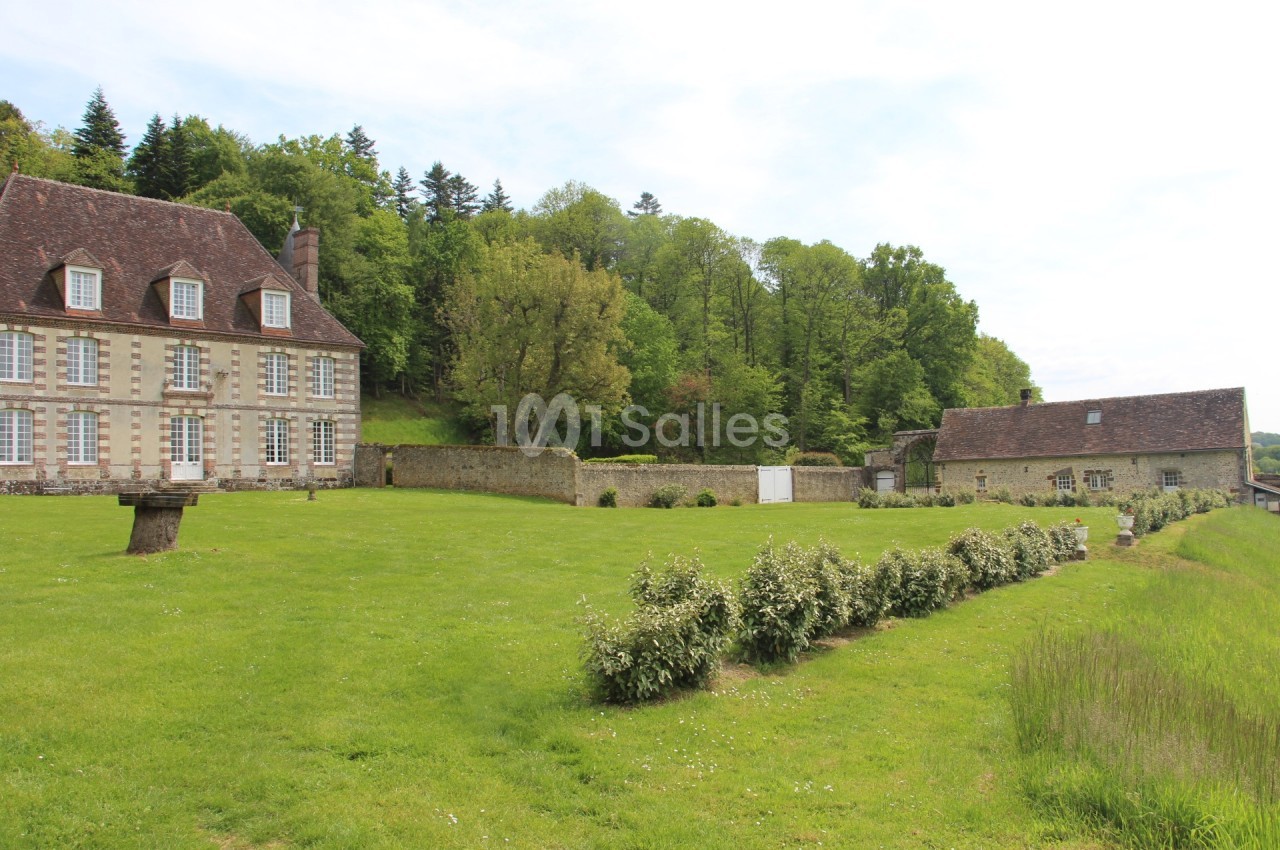 Grande maison en pierre avec toit en ardoise, entourée d'un jardin verdoyant et bordée d'arbres.