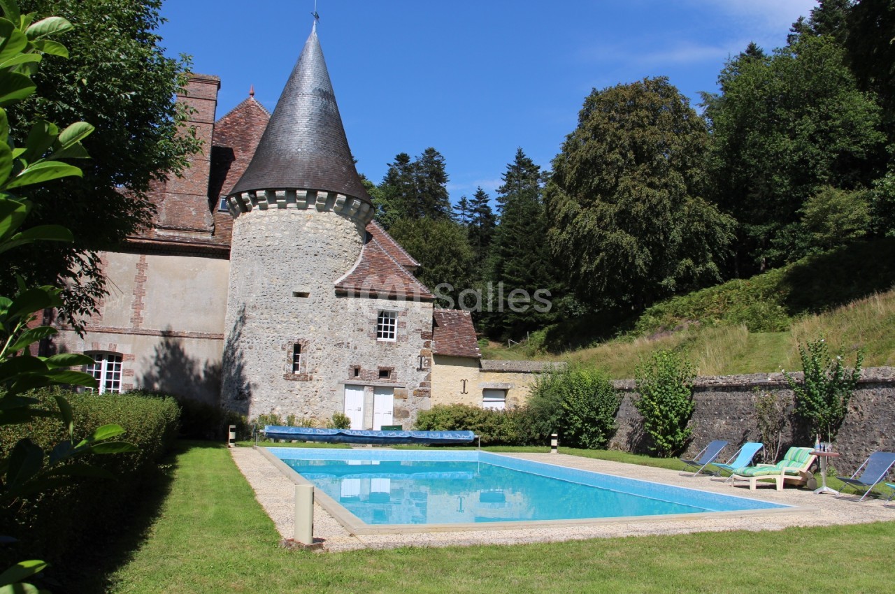 Château en pierre avec une tour ronde, piscine extérieure entourée de chaises longues et jardin arboré.