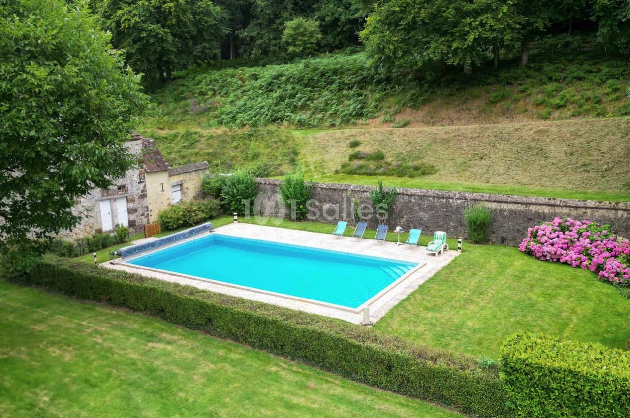 Piscine extérieure rectangulaire entourée de pelouse, de haies taillées et de chaises longues, dans un cadre verdoyant.
