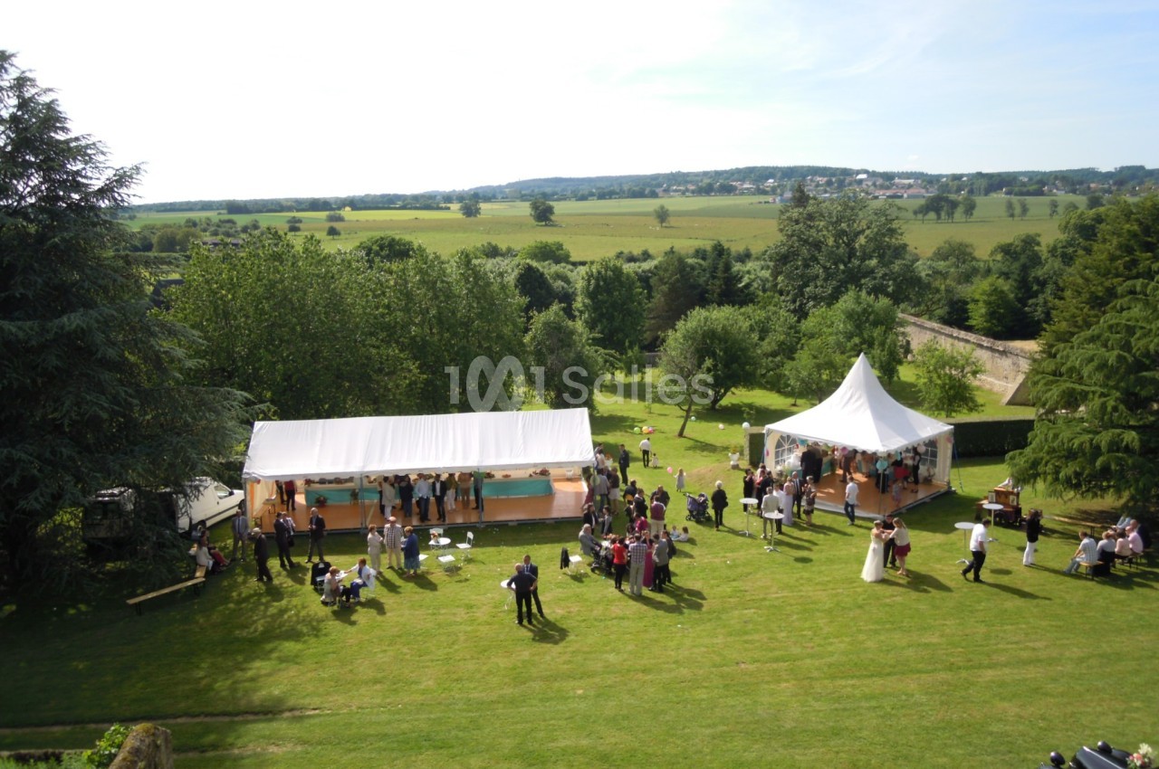 Vue aérienne d'une réception en plein air avec des tentes blanches, des invités et un paysage verdoyant en arrière-plan.