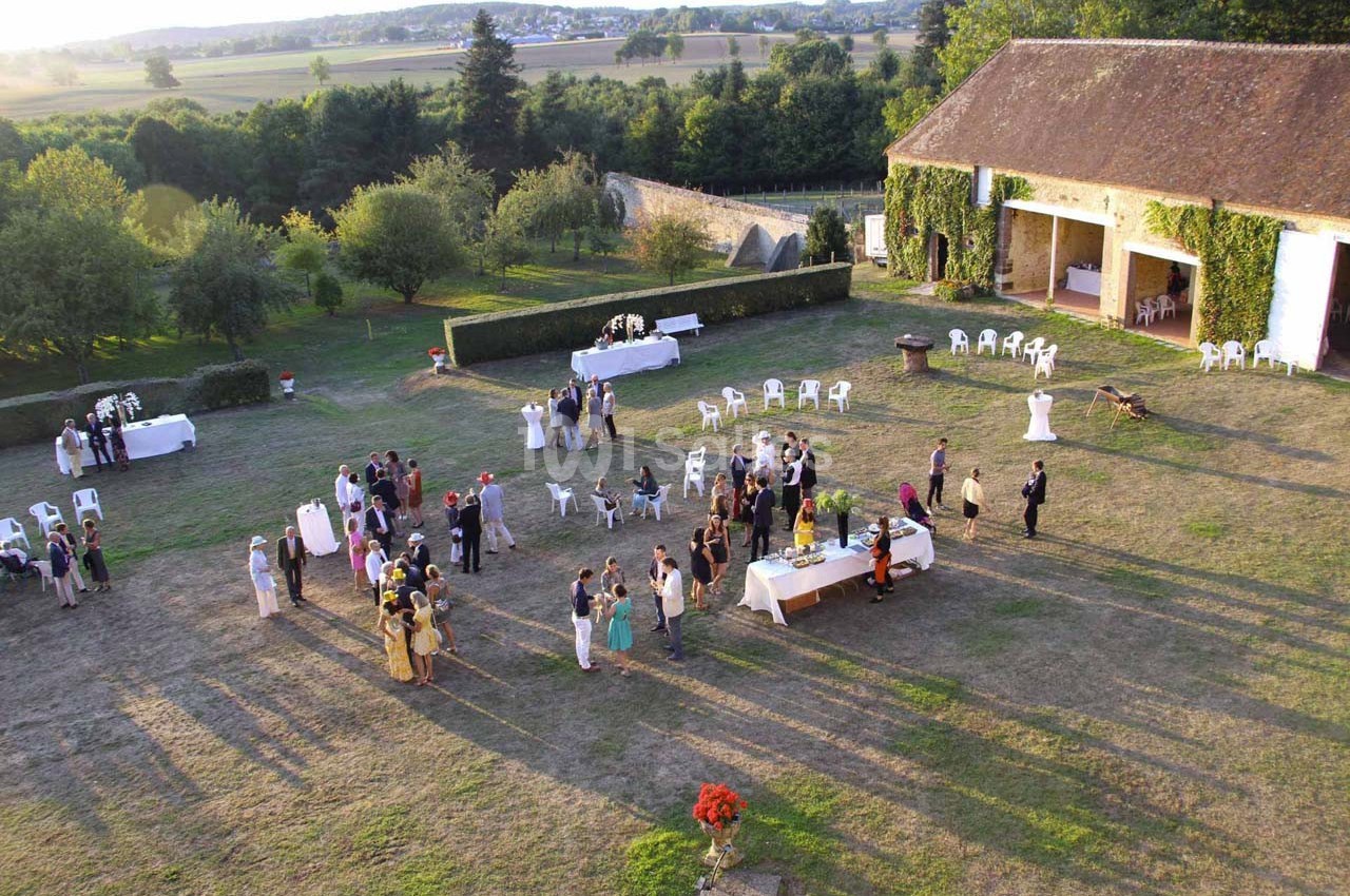 Vue aérienne d'une réception en plein air avec des invités rassemblés autour de tables dans un jardin près d'un bâtiment.